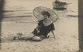 Frau mit Sonnenschirm am Wasser sitzend